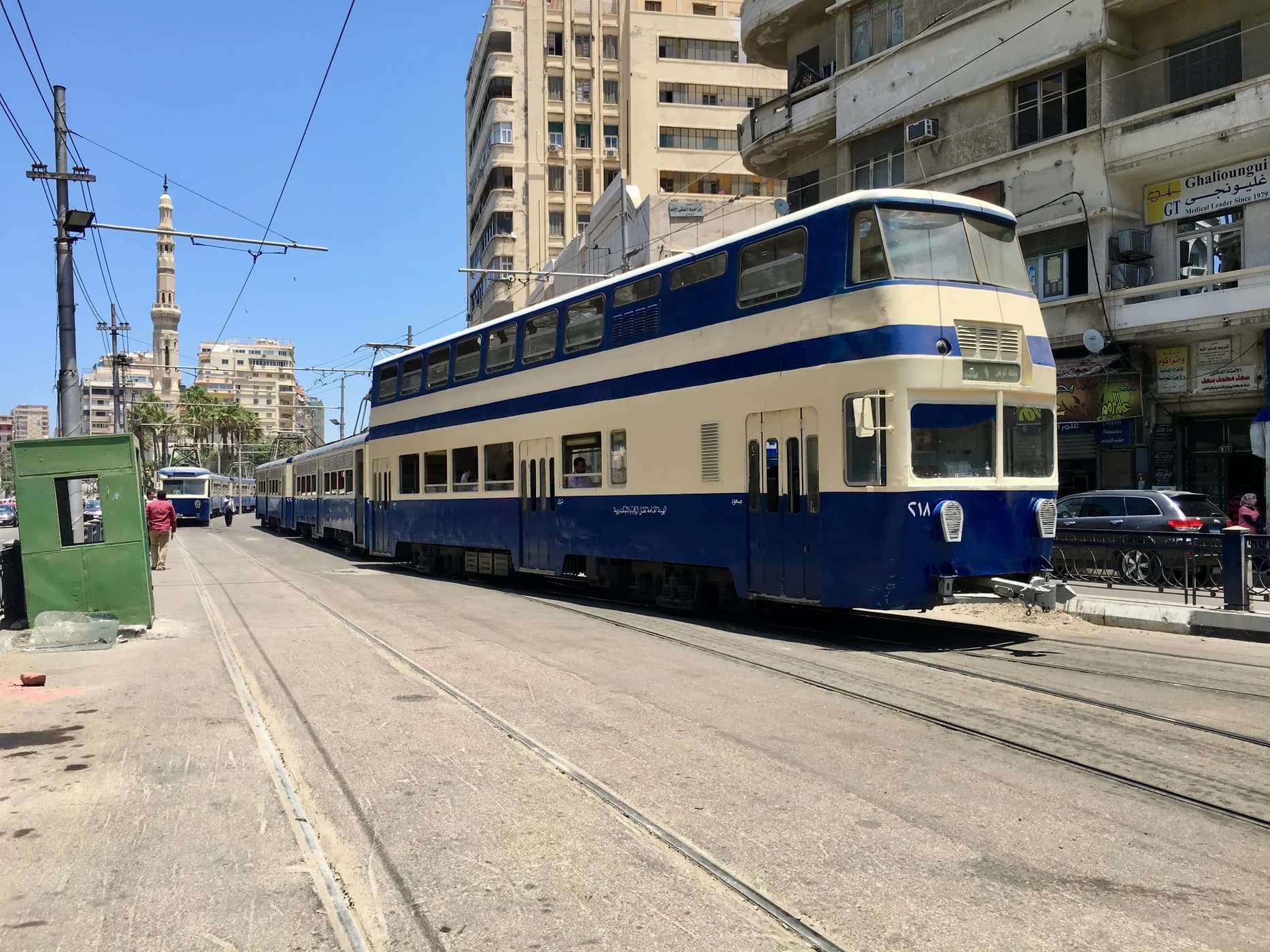 Blue Alexandria tram moving through a busy city street lined with shops