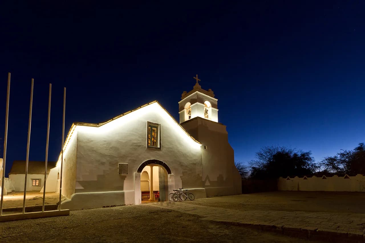 The white adobe Church of San Pedro de Atacama illuminated at dusk beneath a deep blue sky