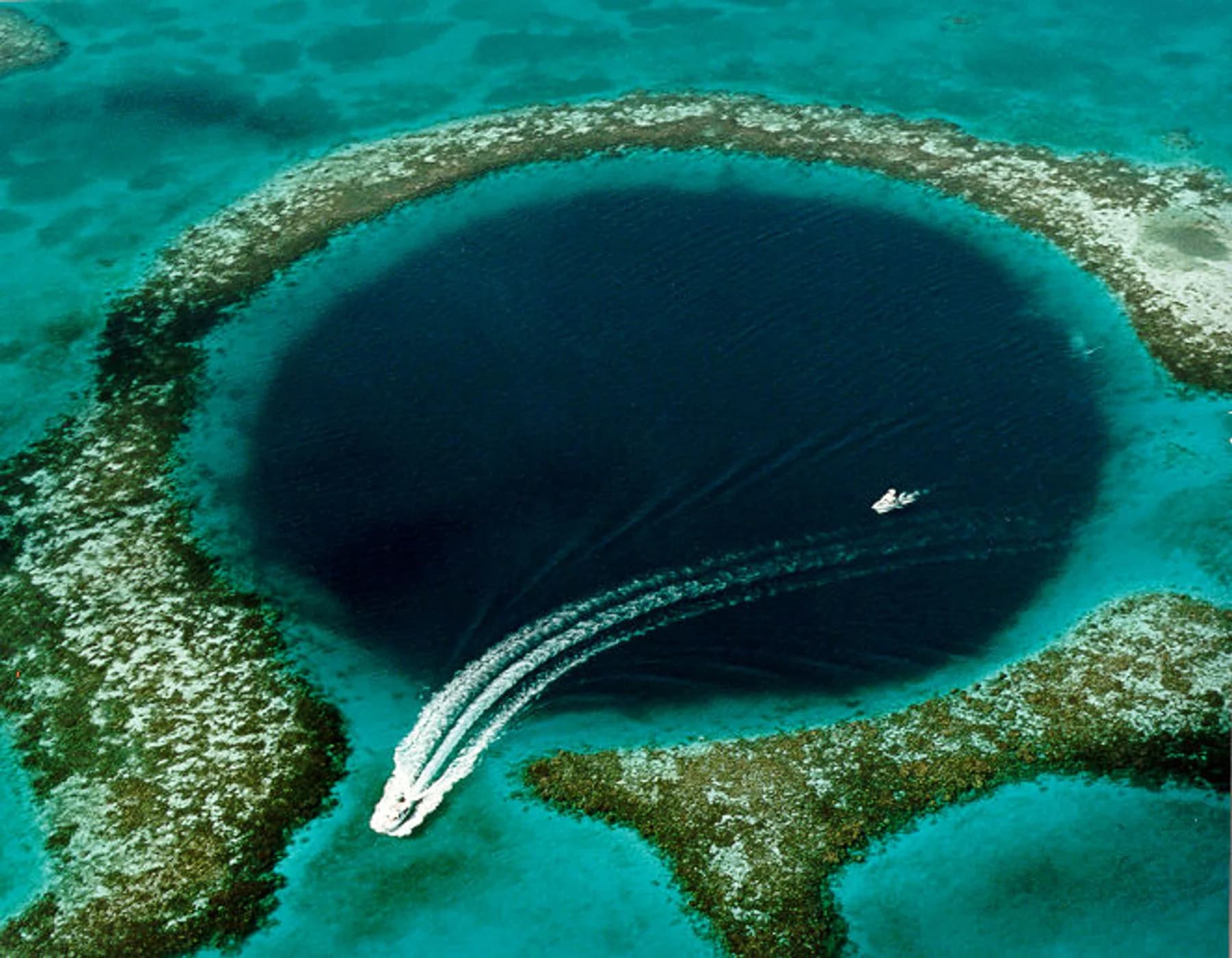 Aerial view of the Great Blue Hole with a small boat crossing the water