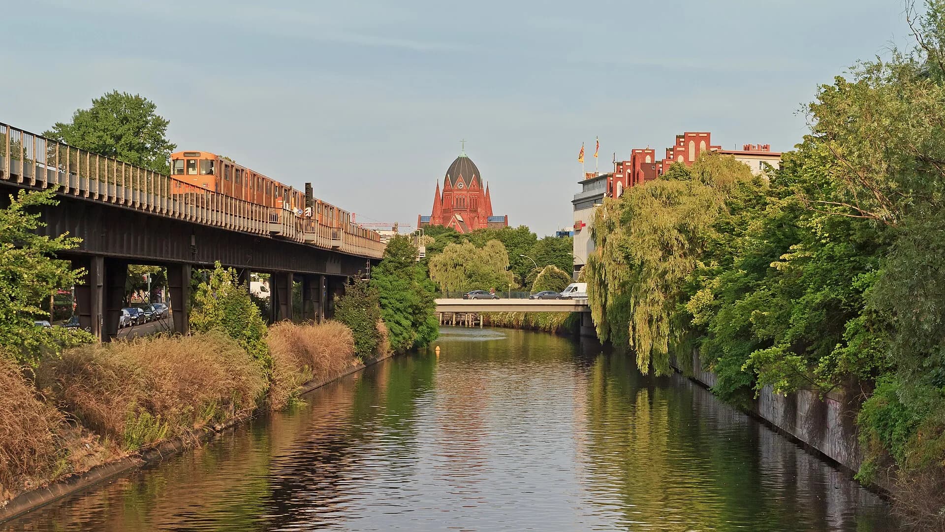 Landwehr Canal in Kreuzberg with trees, a red train, and the city beyond