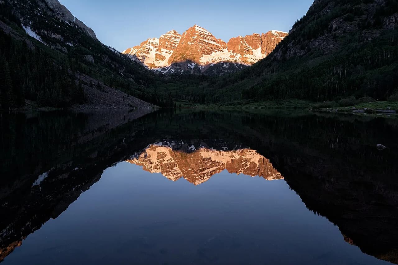 Sunrise lighting the Maroon Bells above their reflection in Maroon Lake near Aspen