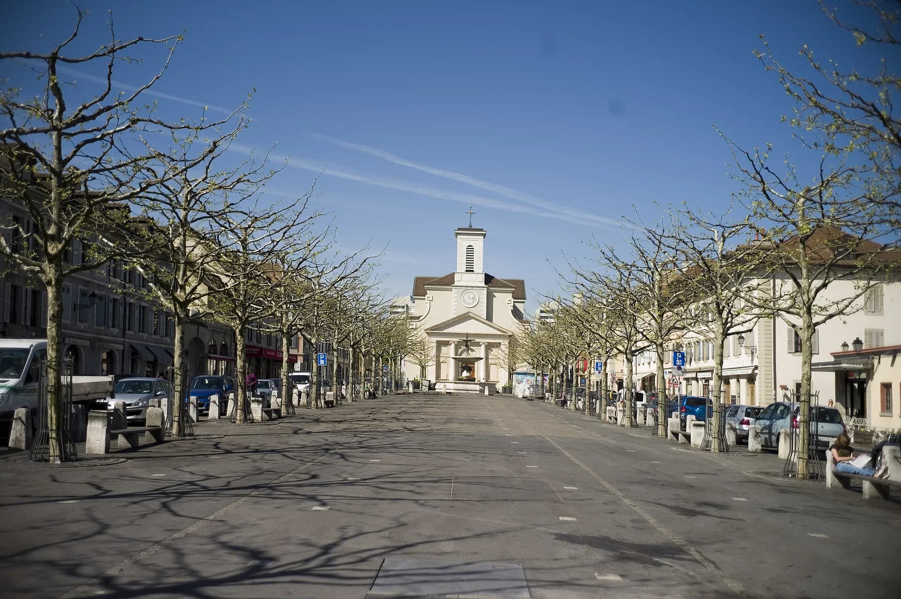 Tree-lined Place du Marché in Carouge with Sainte-Croix church at the end of the street